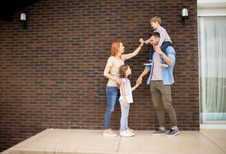 Téléchargez les photos : Famille avec une mère, père, fils et fille debout près du mur d'une maison en brique - en image libre de droit
