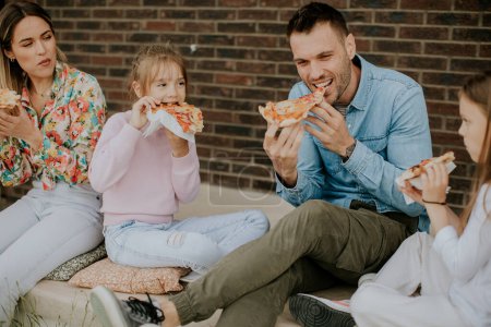 Téléchargez les photos : Heureux groupe de jeunes et d'enfants mangeant de la pizza dans la cour arrière de la maison - en image libre de droit