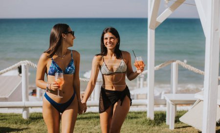 Photo for Two smiling young women in bikini enjoying vacation on the beach while drinking cocktail - Royalty Free Image