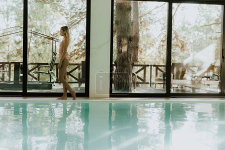 Téléchargez les photos : Jolie jeune femme marchant près de la piscine intérieure - en image libre de droit