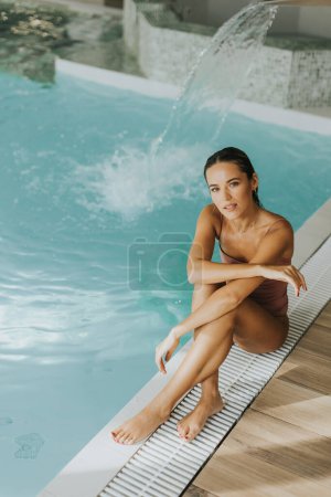 Téléchargez les photos : Jolie jeune femme relaxante au bord de la piscine intérieure - en image libre de droit