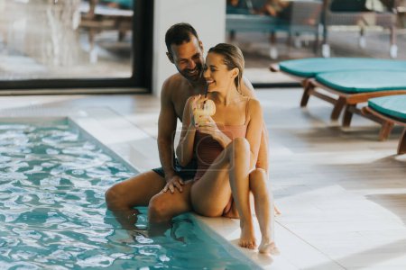 Téléchargez les photos : Beau jeune couple relaxant au bord de la piscine intérieure - en image libre de droit