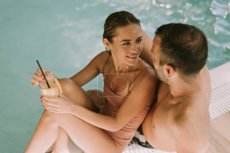 Foto de Hermosa pareja joven relajándose junto a la piscina cubierta - Imagen libre de derechos