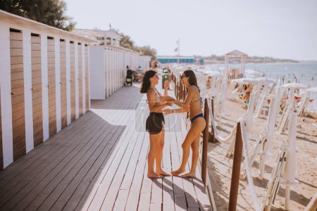 Foto de Dos jóvenes sonrientes en bikini de pie junto a las cabañas y disfrutando de unas vacaciones en la playa - Imagen libre de derechos