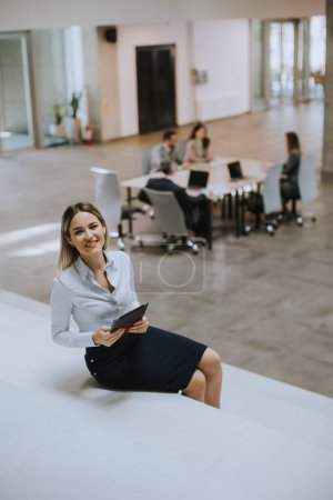 Téléchargez les photos : Jeune femme d'affaires avec tablette numérique debout dans le bureau moderne devant son équipe - en image libre de droit
