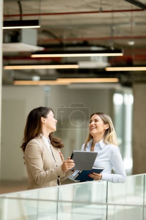 Foto de Dos mujeres de negocios bastante jóvenes con tableta digital en el pasillo de la oficina - Imagen libre de derechos