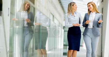 Photo for Two pretty young business women walking and discussing in the office hallway - Royalty Free Image