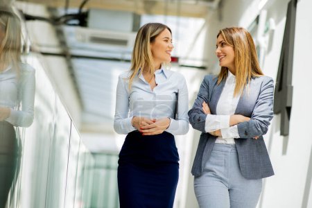 Photo for Two pretty young business women walking and discussing in the office hallway - Royalty Free Image