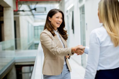 Photo for Two pretty young business women handshaking in the office hallway - Royalty Free Image