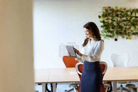 Téléchargez les photos : Jeune femme d'affaires avec tablette numérique debout dans le bureau moderne - en image libre de droit