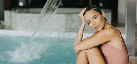 Photo for Pretty young woman relaxing by the indoor swimming pool - Royalty Free Image