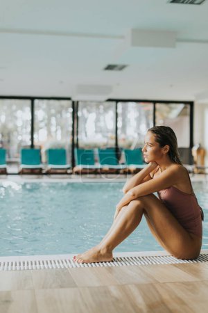 Photo for Pretty young woman relaxing by the indoor swimming pool - Royalty Free Image