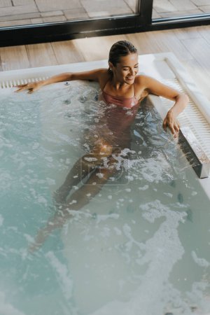 Téléchargez les photos : Jolie jeune femme relaxante dans la piscine à bulles intérieure - en image libre de droit