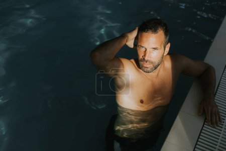 Photo for Handsome young man relaxing on the edge of a indoor swimming pool - Royalty Free Image