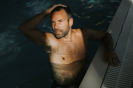 Foto de Joven guapo relajándose en el borde de una piscina cubierta - Imagen libre de derechos