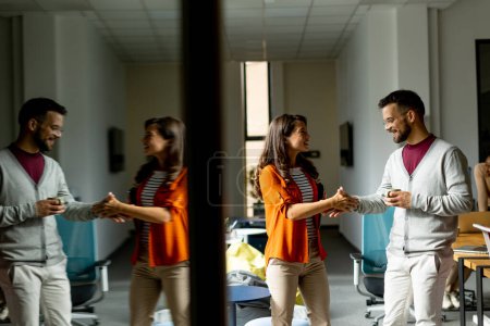 Photo for Young business couple standing and handshaking in front of her team at the modern office - Royalty Free Image