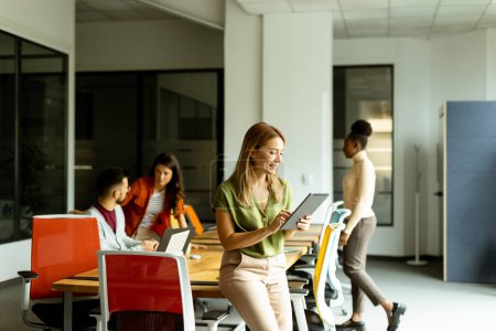 Téléchargez les photos : Jeune femme debout avec tablette numérique devant son équipe au bureau moderne - en image libre de droit
