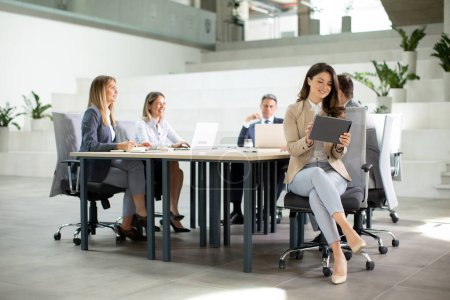 Téléchargez les photos : Jeune femme d'affaires avec tablette numérique dans le bureau moderne devant son équipe - en image libre de droit