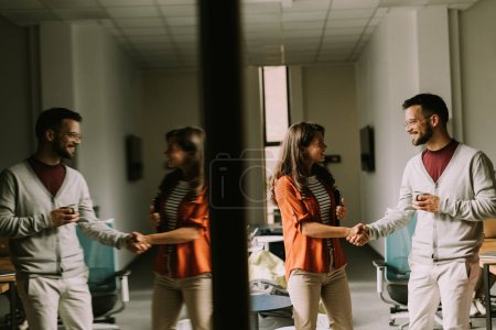 Foto de Joven pareja de negocios de pie y apretón de manos delante de su equipo en la oficina moderna - Imagen libre de derechos