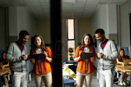 Téléchargez les photos : Jeune couple d'affaires debout avec tablette numérique devant son équipe au bureau moderne - en image libre de droit