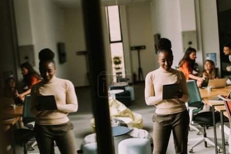Téléchargez les photos : Jeune femme afro-américaine debout avec tablette numérique devant son équipe au bureau moderne - en image libre de droit