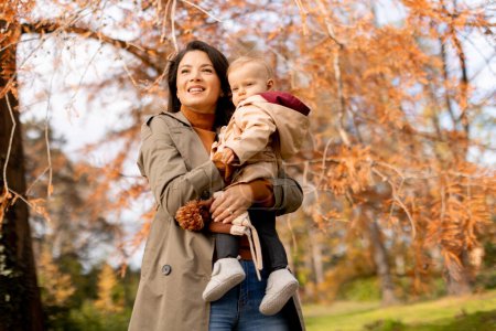 Photo for Young woman holding a cute baby girl in the autumn park - Royalty Free Image