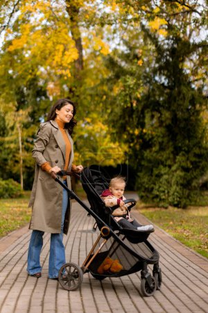 Foto de Mujer joven con una linda niña en el cochecito de bebé en el parque de otoño - Imagen libre de derechos