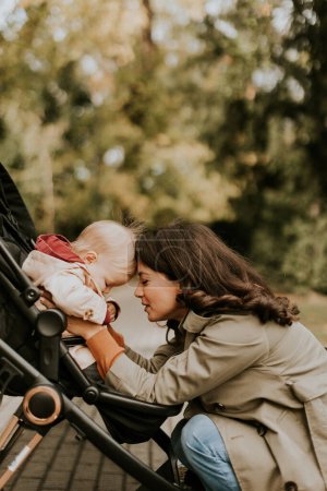 Foto de Mujer joven con una linda niña en el cochecito de bebé en el parque de otoño - Imagen libre de derechos