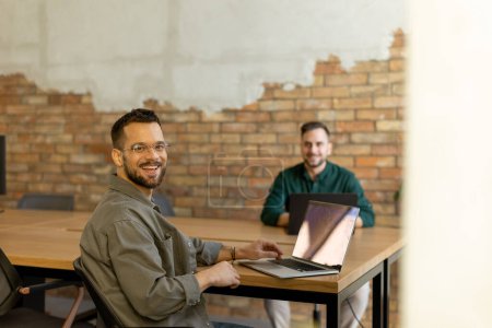 Téléchargez les photos : Deux professionnels souriants s'engagent dans une séance de travail collaboratif à une table en bois, leur camaraderie évidente dans un cadre de bureau contemporain avec une toile de fond murale en brique exposée - en image libre de droit