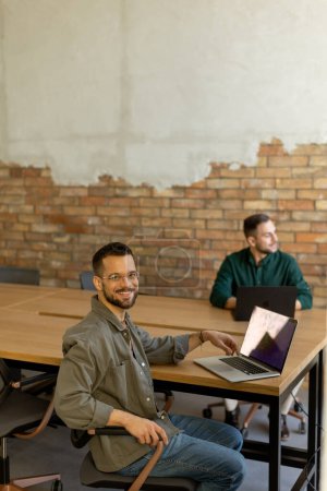 Téléchargez les photos : Deux professionnels souriants s'engagent dans une séance de travail collaboratif à une table en bois, leur camaraderie évidente dans un cadre de bureau contemporain avec une toile de fond murale en brique exposée - en image libre de droit