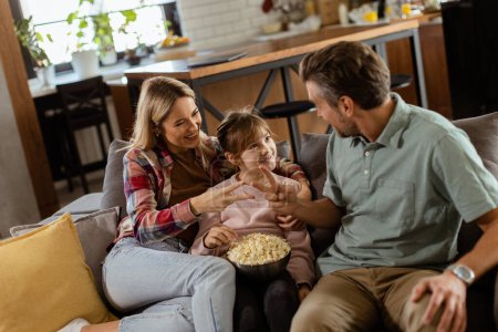 Photo for A joyful family lounges on the sofa, engaging in playful conversation with a bowl of popcorn - Royalty Free Image