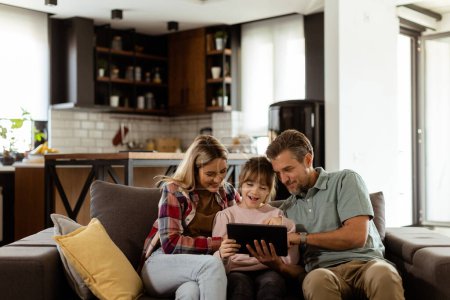 Photo for Joyful family shares a moment around a digital tablet, with smiles and togetherness in a warm home setting - Royalty Free Image