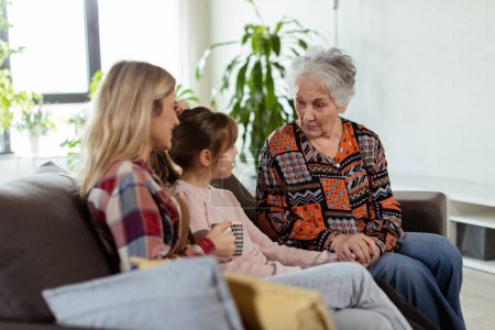 Three generations of women enjoy laughter and conversation on a comfortable living room couch