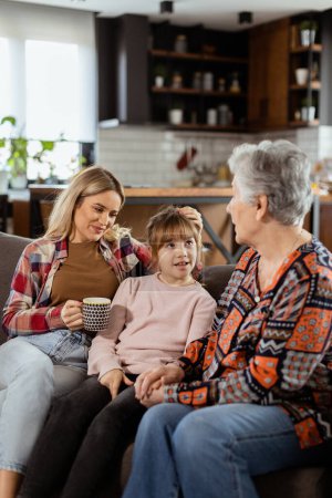 Tres generaciones de mujeres disfrutan de la risa y la conversación en un cómodo sofá de sala de estar