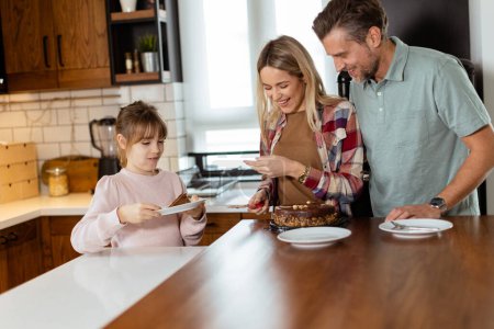 Foto de Una conmovedora escena se desarrolla mientras una familia disfruta de un delicioso pastel de chocolate juntos en el calor de su cocina iluminada por el sol, compartiendo sonrisas y creando recuerdos. - Imagen libre de derechos
