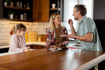 Photo for A heartwarming scene unfolds as a family relishes a mouthwatering chocolate cake together in the warmth of their sunlit kitchen, sharing smiles and creating memories - Royalty Free Image