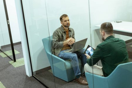 Photo for Two professionals engage in a conversation while seated comfortably in an office lounge, surrounded by greenery and contemporary design elements - Royalty Free Image