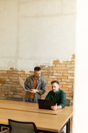 Two smiling professionals engage in a collaborative work session at a wooden table, their camaraderie evident in a contemporary office setting with an exposed brick wall backdrop