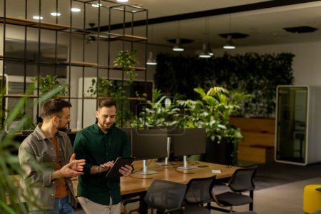 Foto de Dos profesionales se dedican a una conversación enfocada mientras sostienen la tableta digital en un espacio de oficina contemporáneo, con ladrillos expuestos rústicos y luz natural cálida - Imagen libre de derechos