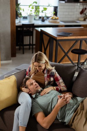 Couple partage un moment tendre et paisible que l'un repose leur tête sur les autres genoux, entouré par la chaleur et le confort de leur salon.