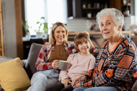 Three generations of women enjoy laughter and conversation on a comfortable living room couch