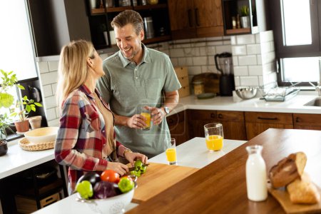 Photo for A pair enjoying a lighthearted conversation with fresh juice and a healthy breakfast spread on the counter. - Royalty Free Image