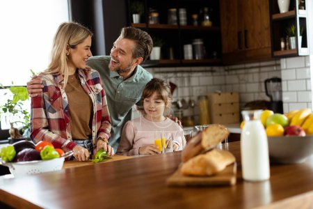 Foto de La familia comparte una sonrisa mientras preparan el desayuno juntos en una acogedora cocina bien iluminada - Imagen libre de derechos