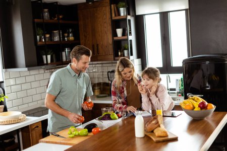 Photo for Young family chatting and preparing food around a bustling kitchen counter filled with fresh ingredients and cooking utensils - Royalty Free Image