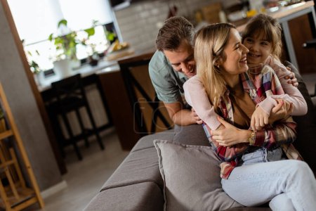Téléchargez les photos : Une famille joyeuse partage un moment détendu et affectueux sur le canapé, illuminé par une douce lumière naturelle - en image libre de droit