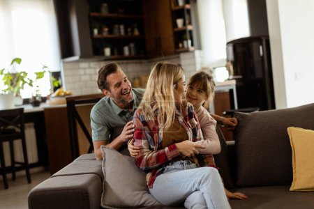 Téléchargez les photos : Une famille joyeuse partage un moment détendu et affectueux sur le canapé, illuminé par une douce lumière naturelle - en image libre de droit