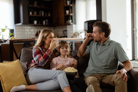Photo for A joyful family lounges on the sofa, engaging in playful conversation with a bowl of popcorn - Royalty Free Image