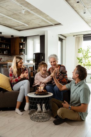 Foto de Escena conmovedora se desarrolla como una familia multigeneracional se reúne en un sofá para presentar un pastel de cumpleaños a una abuela encantada, creando recuerdos para apreciar - Imagen libre de derechos
