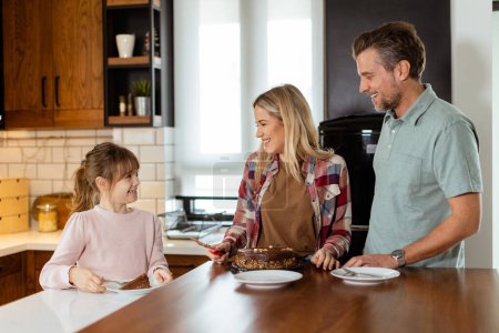 Téléchargez les photos : Une scène chaleureuse se déroule alors qu'une famille savoure un délicieux gâteau au chocolat dans la chaleur de sa cuisine ensoleillée, partageant des sourires et créant des souvenirs - en image libre de droit