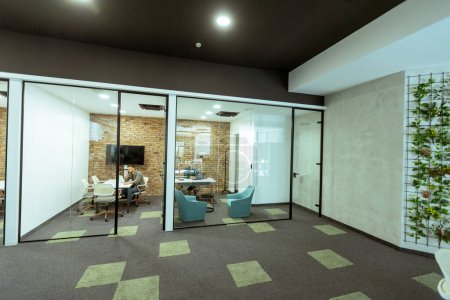 Photo for Person is immersed in a task in a stylish office with transparent glass walls. The modern design includes exposed brick, a sleek monitor, comfortable seating, and an atmosphere of quiet productivity. This scene captures a moment of dedicated work in - Royalty Free Image